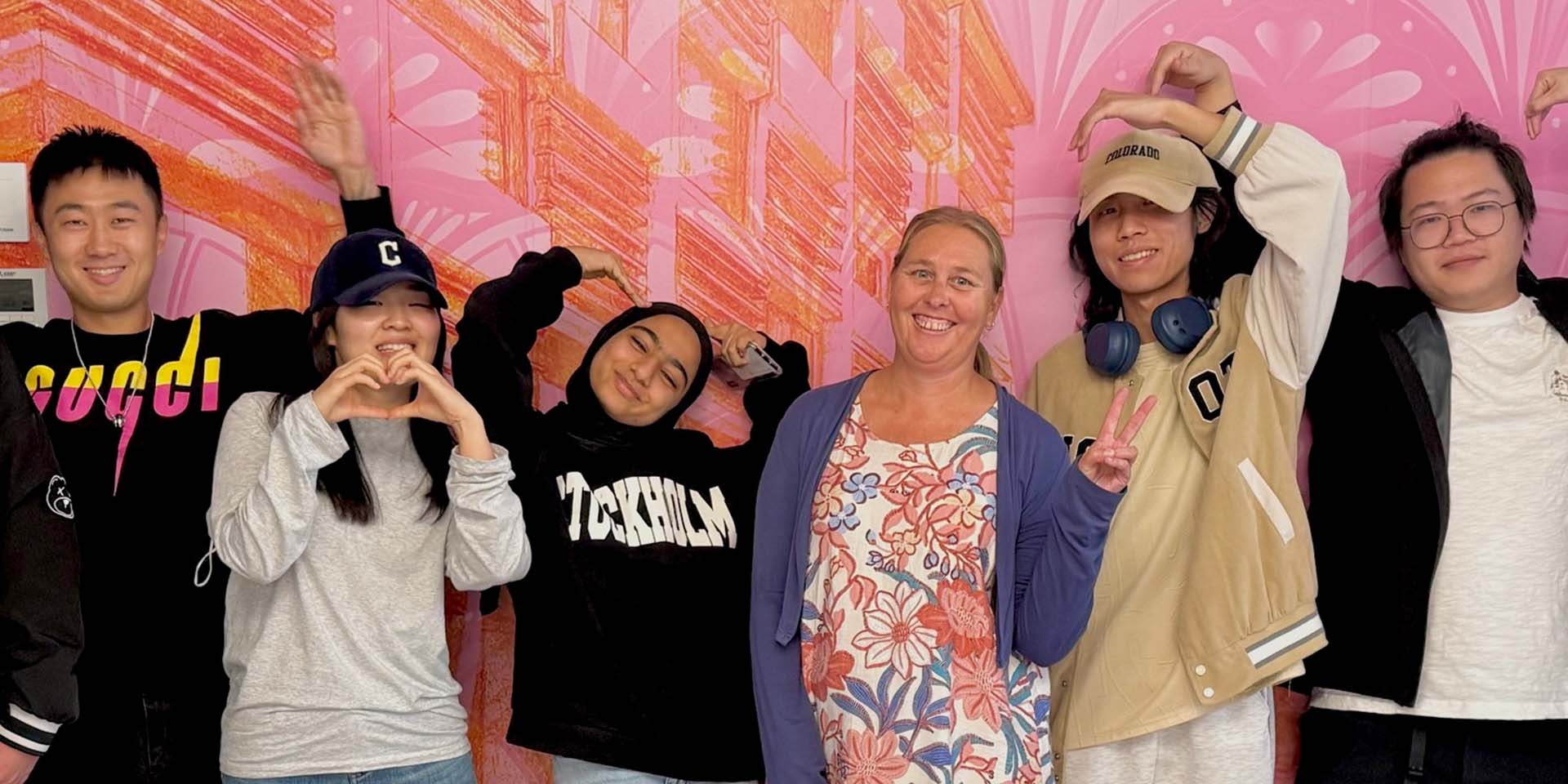A group of 5 international students smiling with their teacher against a bright wall