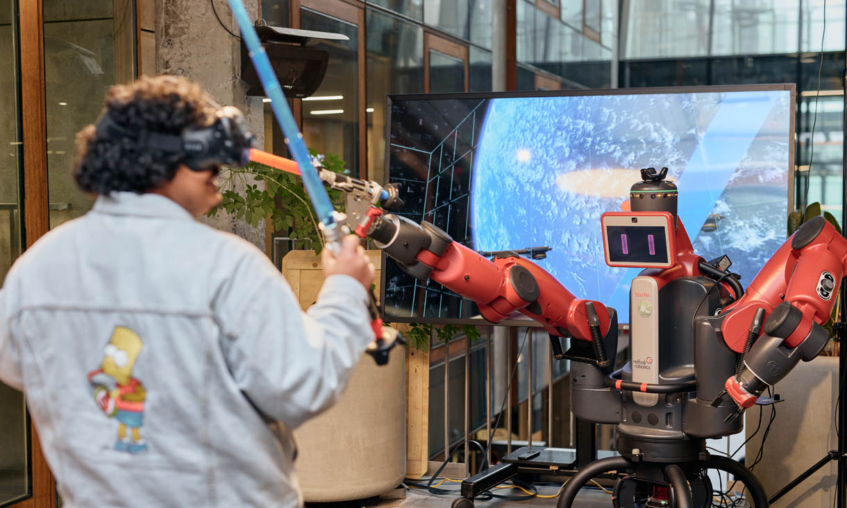 A student wearing a VR headset battles a robot with a light sabre