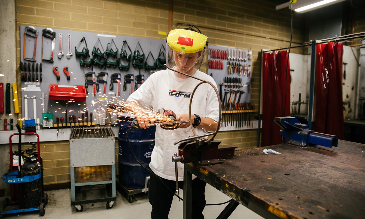 A young student using a grinder on stool frame in a workshop