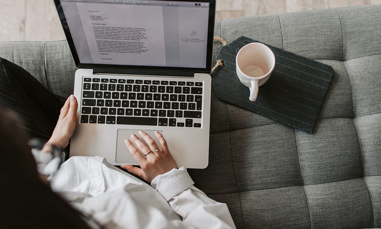 A person sitting on a couch working on a laptop, with a mug next to them