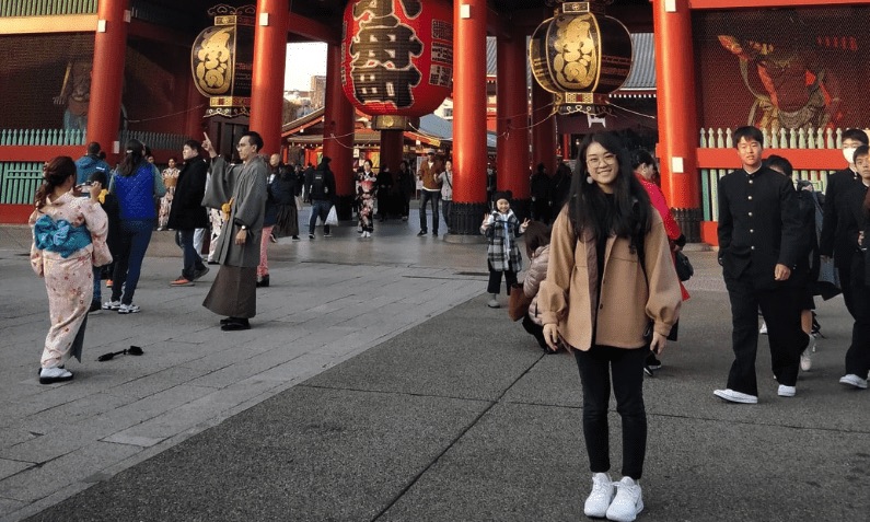 Female student standing in front of red temple