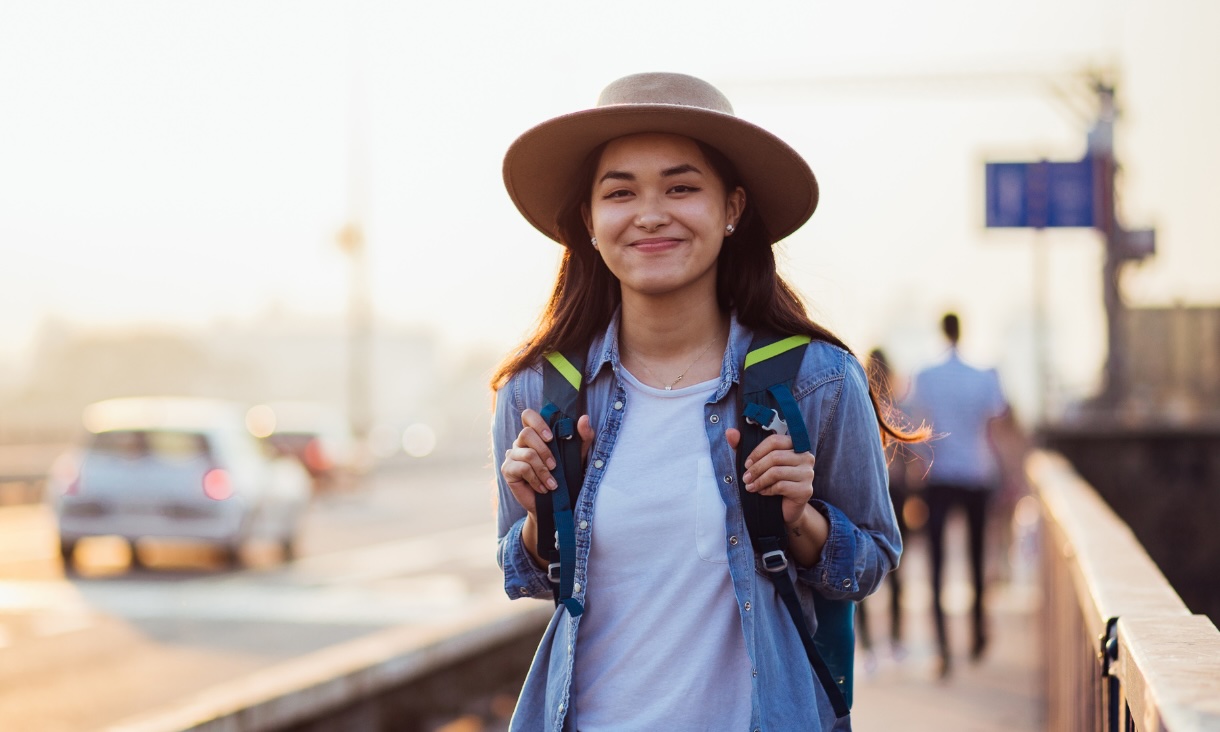 Young woman wearing a wide brimmed hat and backpack smiles at the camera