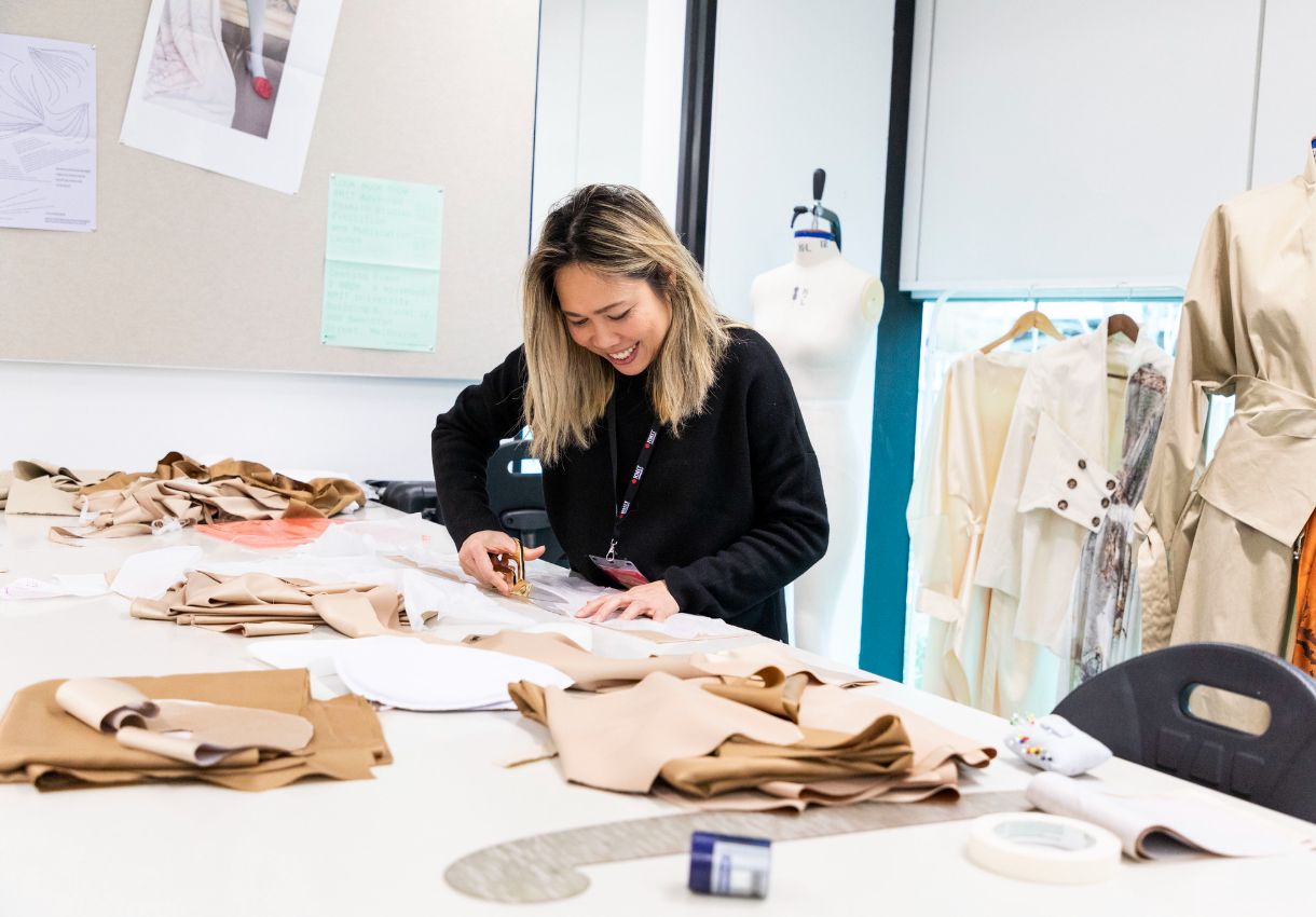 Student standing in a fashion studio cutting fabric.