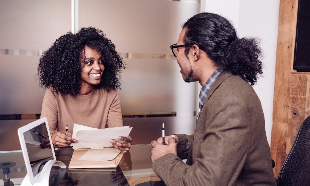 Student holding papers smiles at a Career Consultant with a laptop.