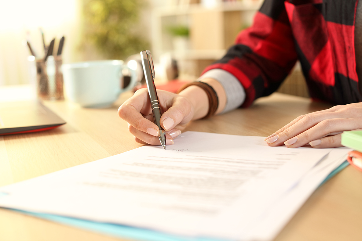 Close up of student girl hands signing contract on a desk at home.