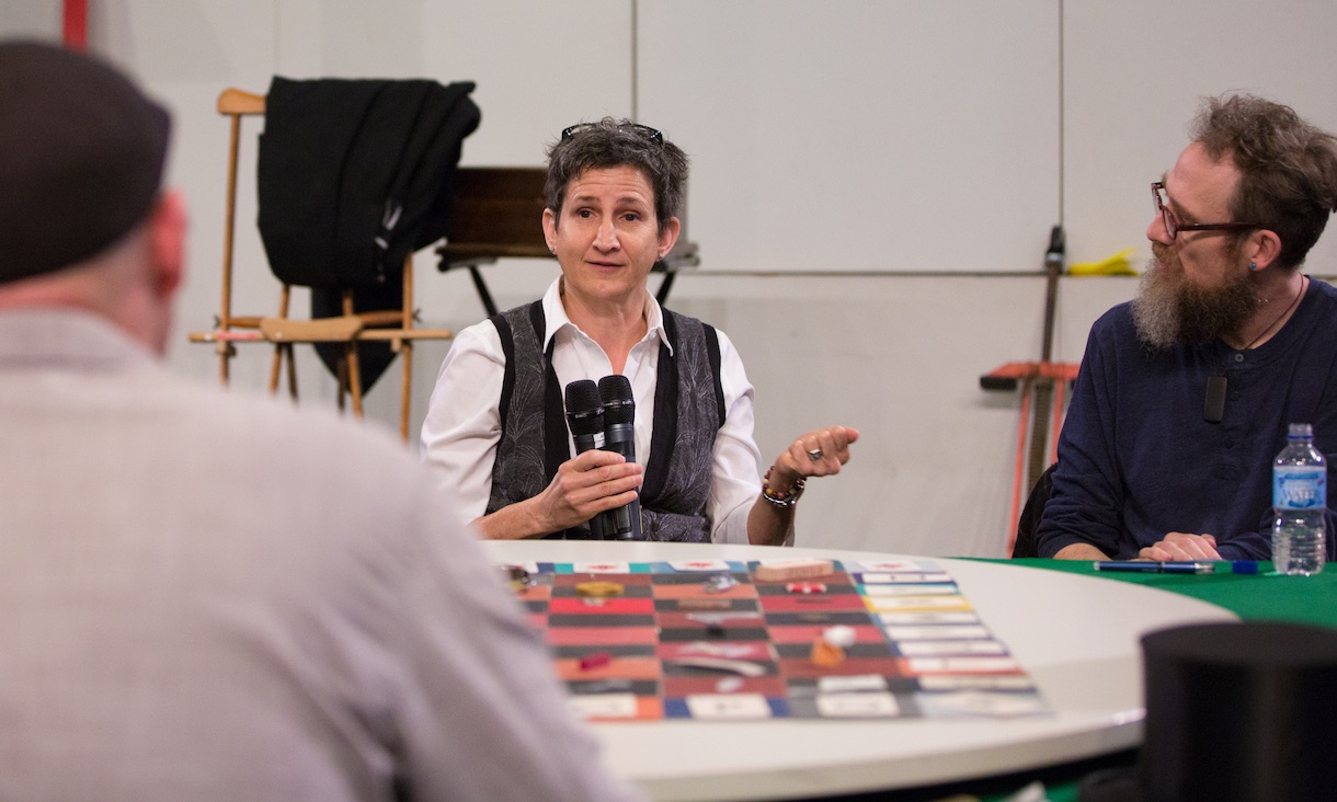 A lecturer with microphone speaks to two students at a table.