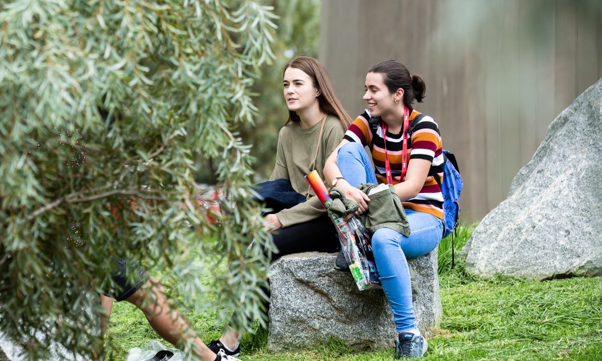 Girls sit near tree.