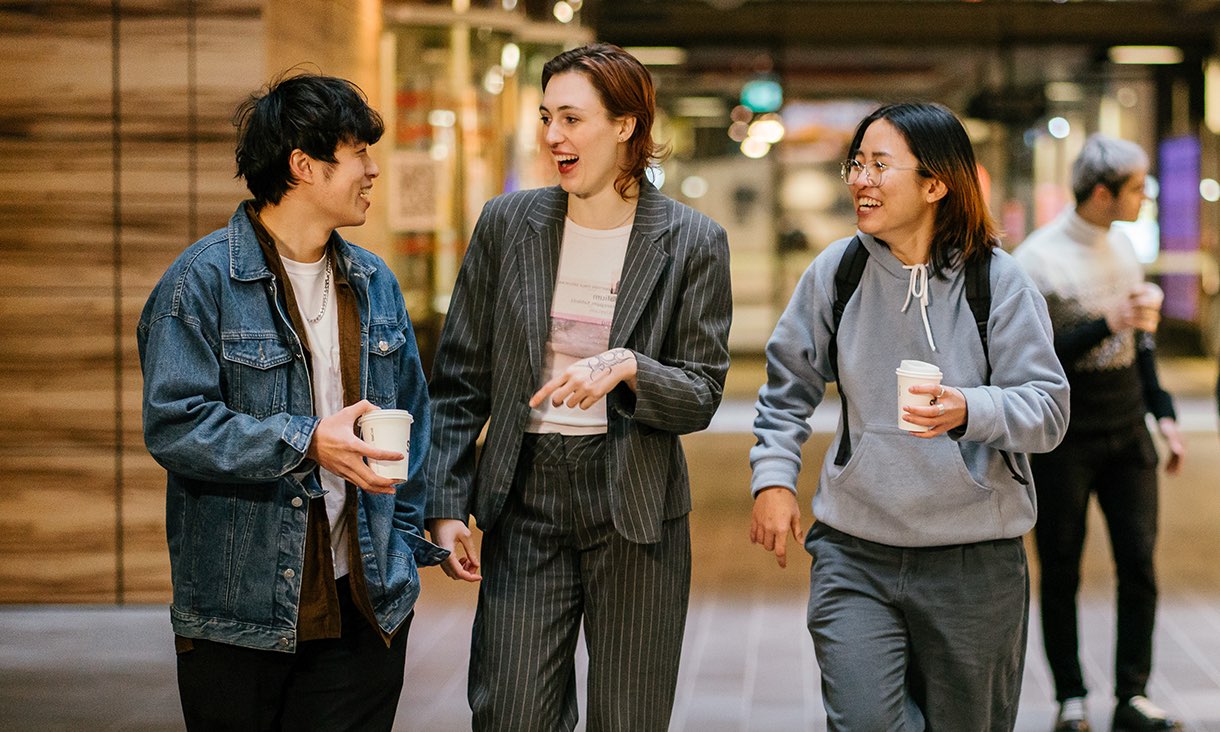 Three students smile as they walk down a corridor.