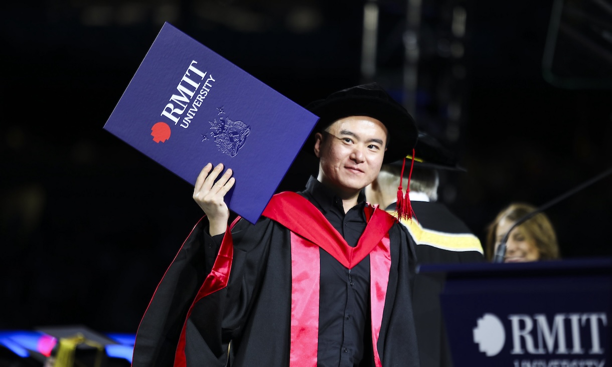 PhD graduate holds up their testamur.