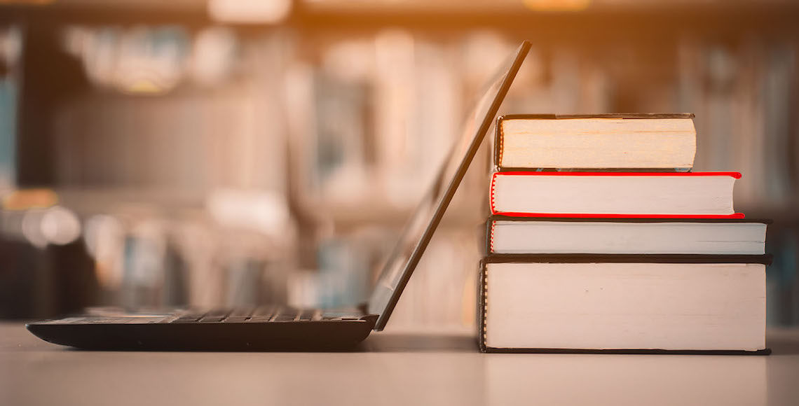 Laptop sitting beside a pile of books