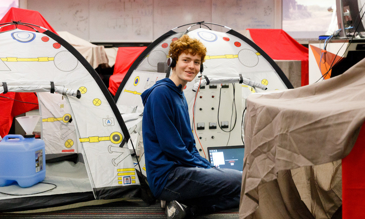 Student sits on campus, surrounded by tents.