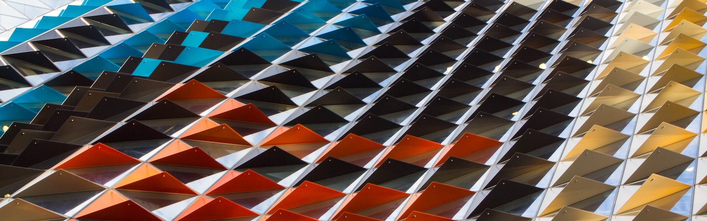 Close-up view of a modern building facade featuring geometric panels in blue, black, orange, and yellow arranged in a striking pattern.