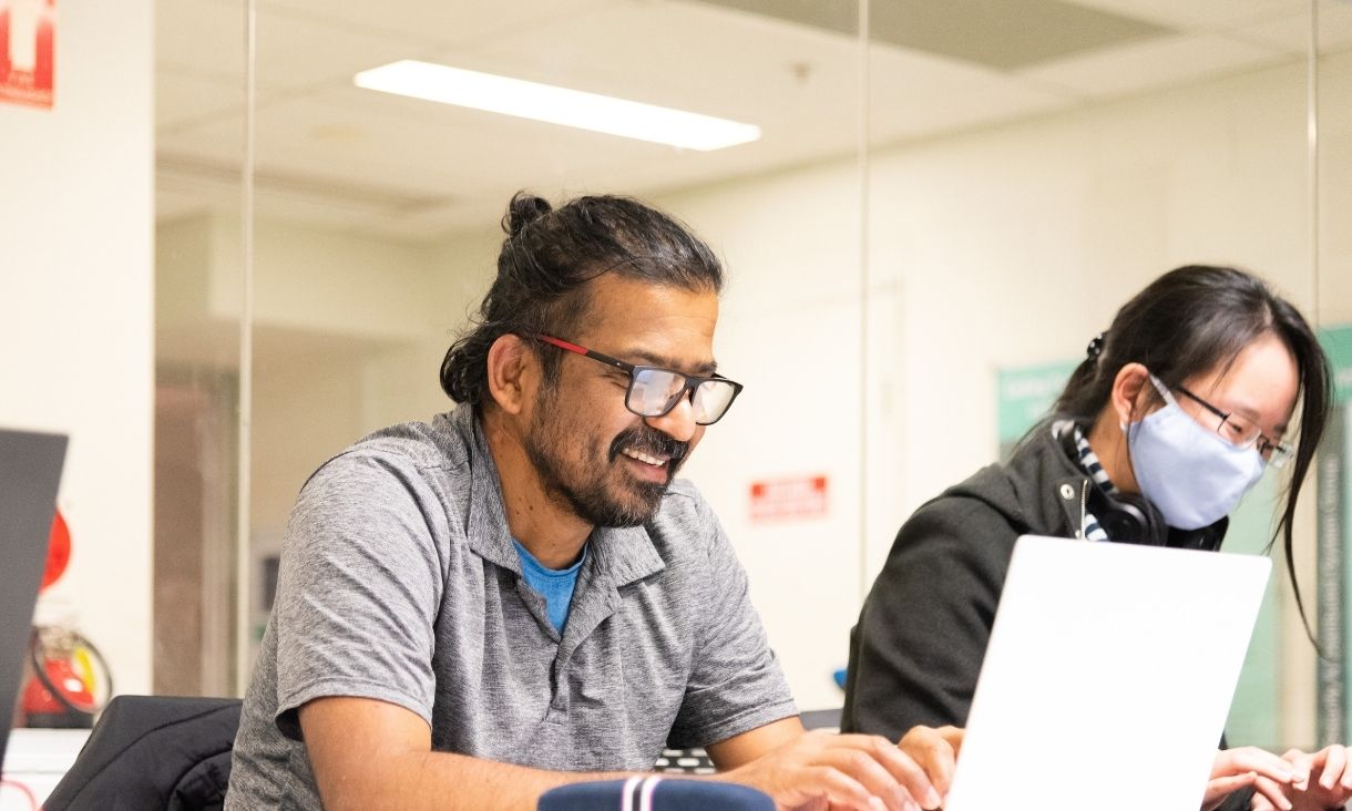 A man works at a laptop in a classroom.