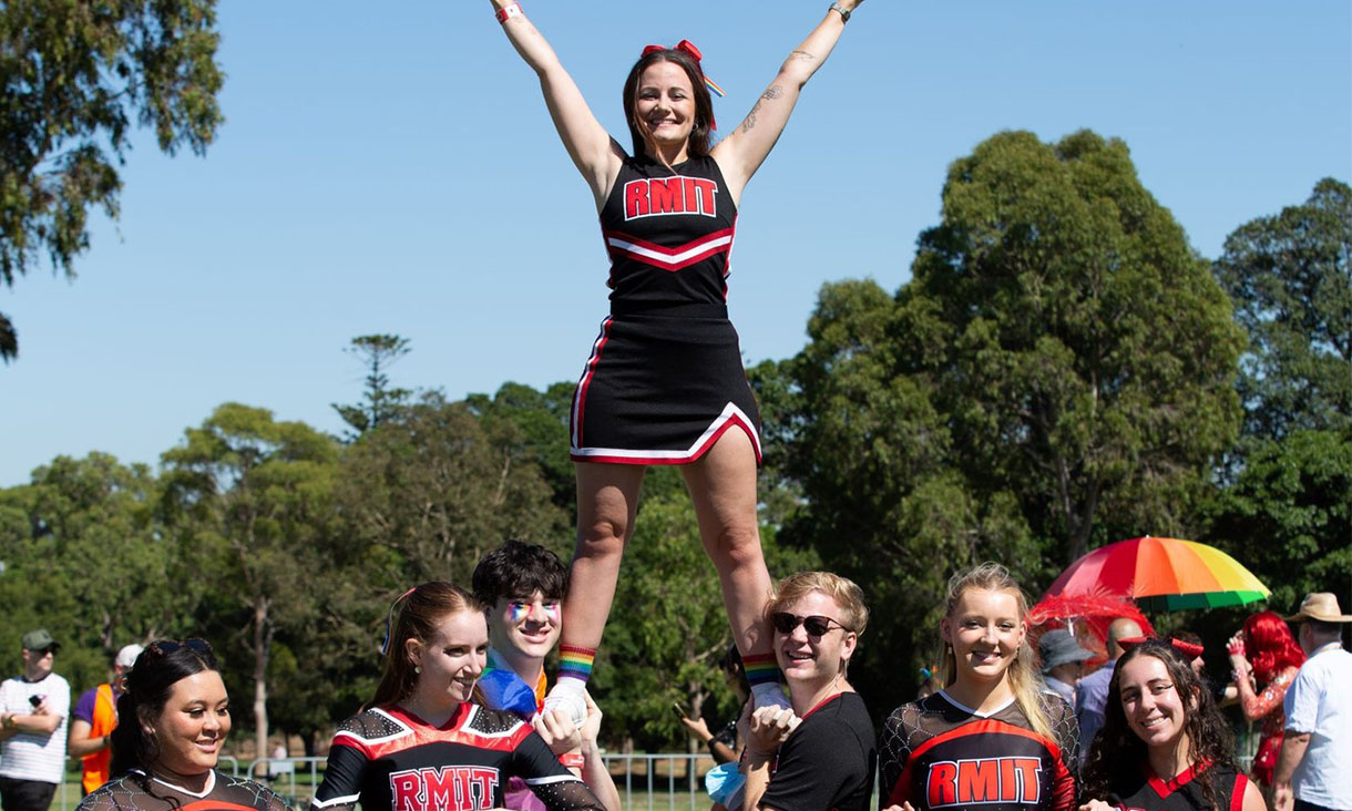 Group of students smiling at camera while holding female cheerleader