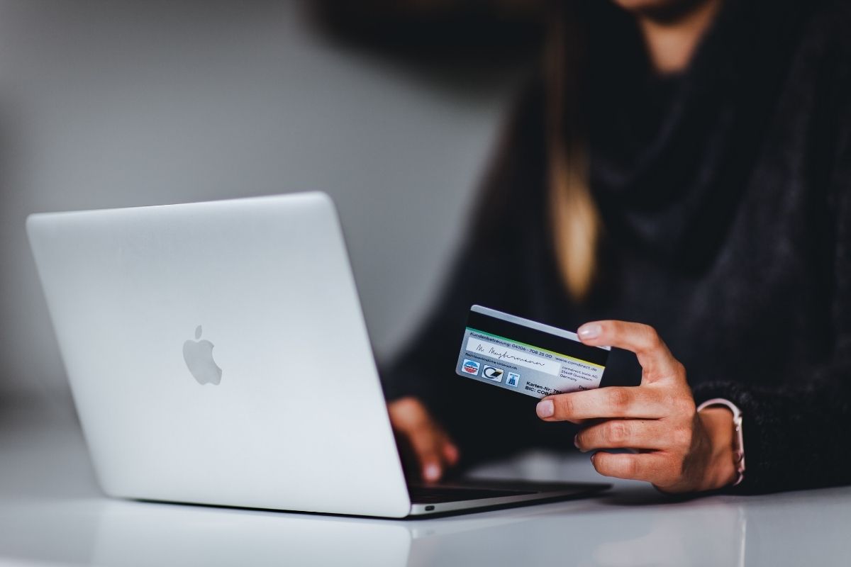 A person holds a credit card and writes on their laptop.