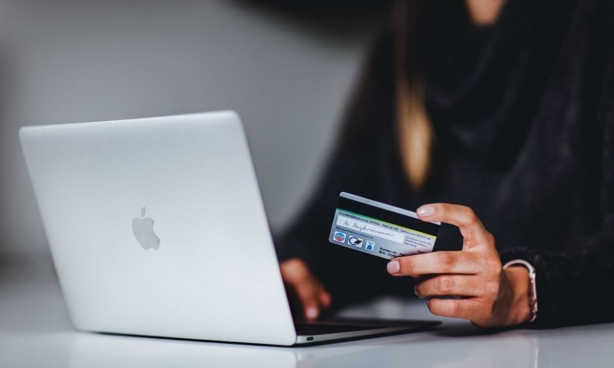 A person types on a laptop on a desk and holds a credit card.