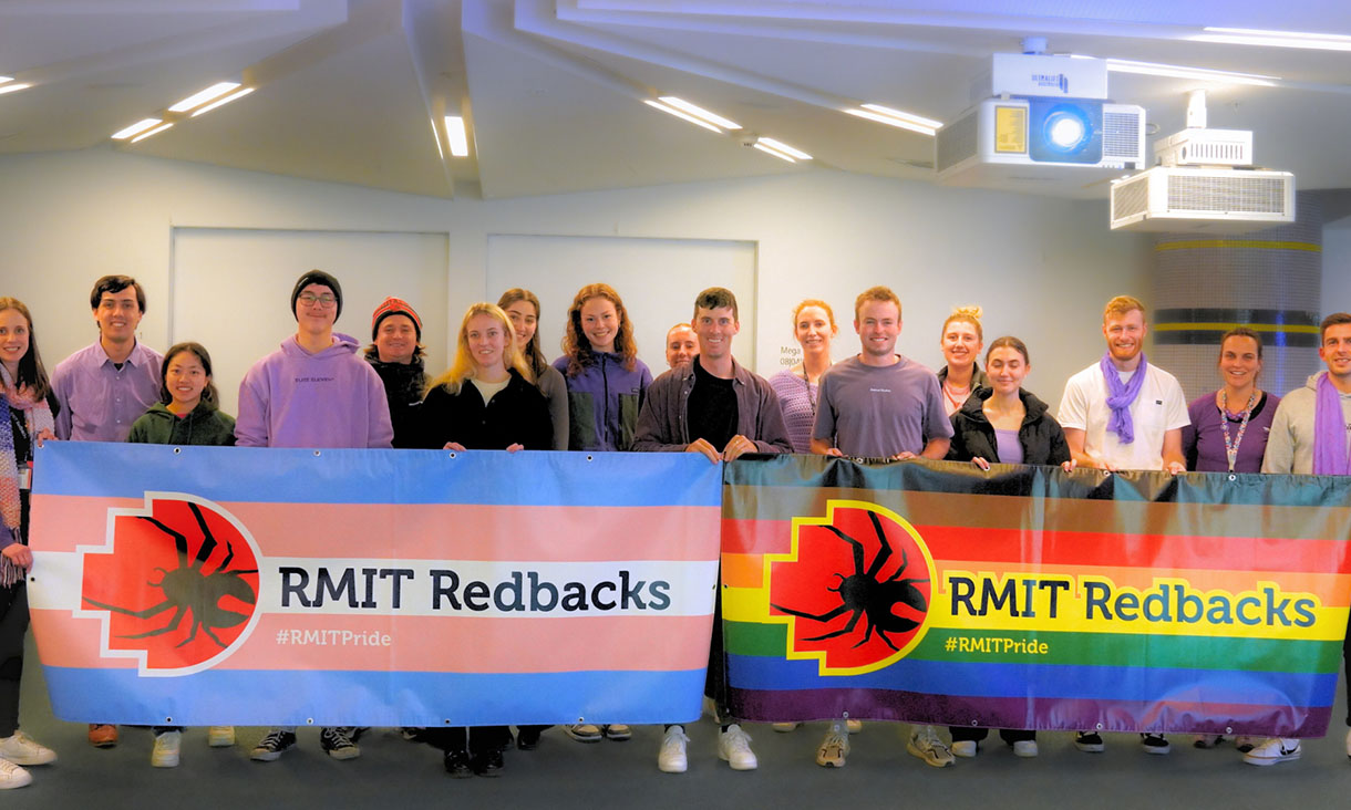 Group wearing purple behind pride themed banners.