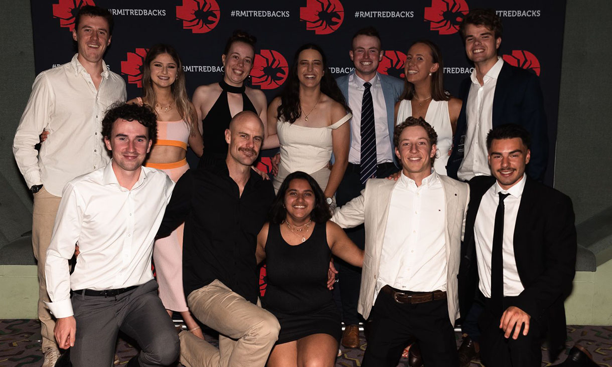Group of people pose for photo in front of a black and red banner