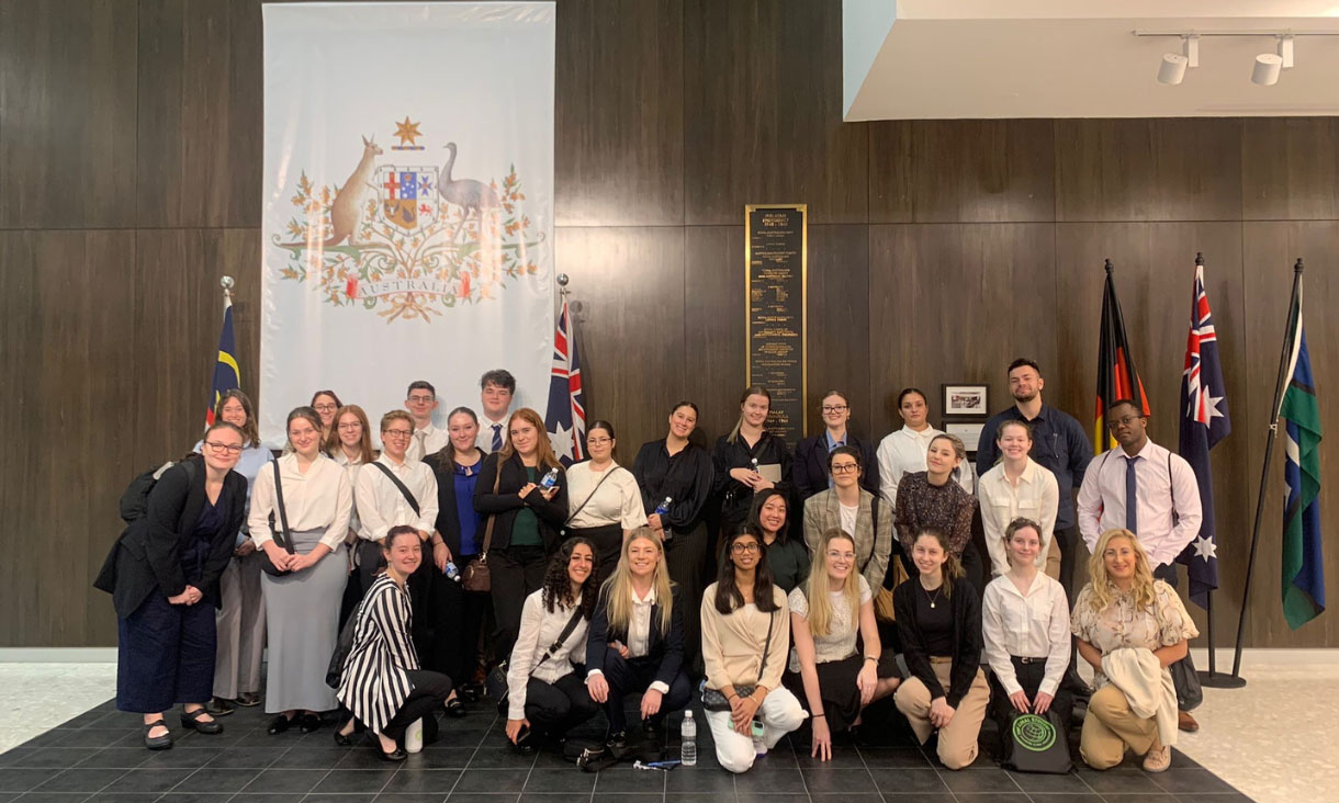 Group of people standing in front f Australian Coat of Arms