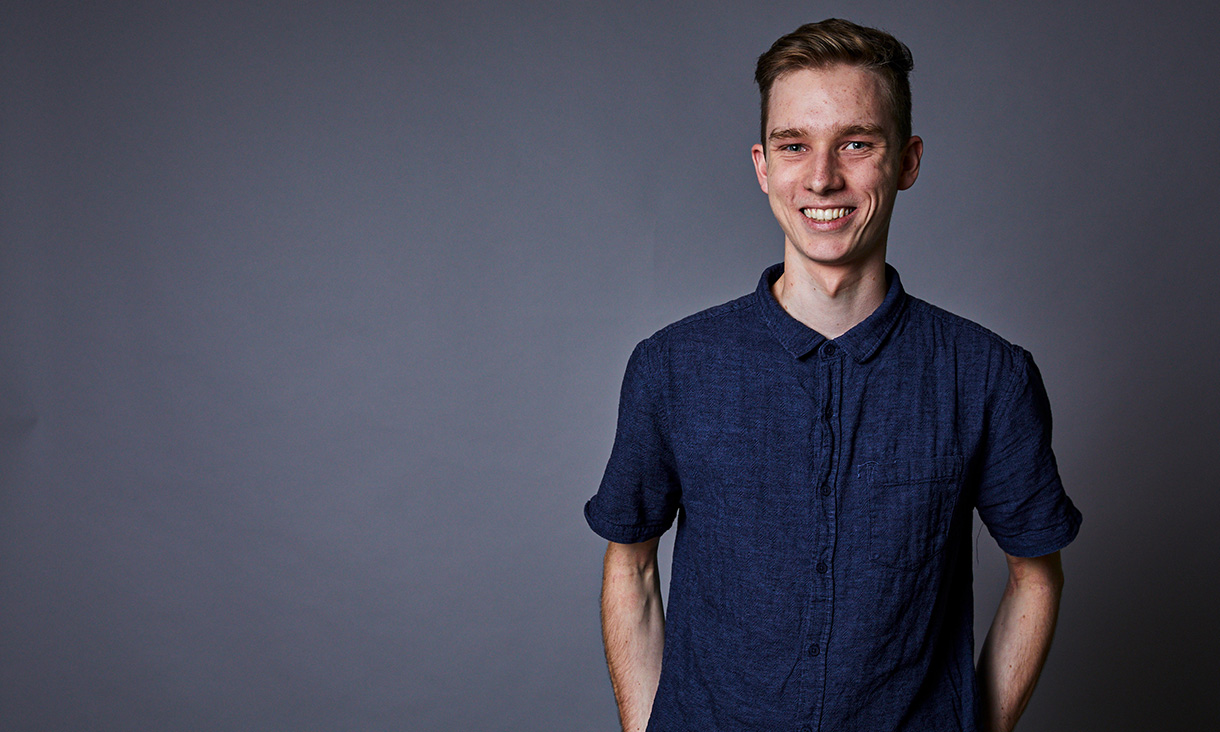 A student in a blue shirt smiles for a photograph