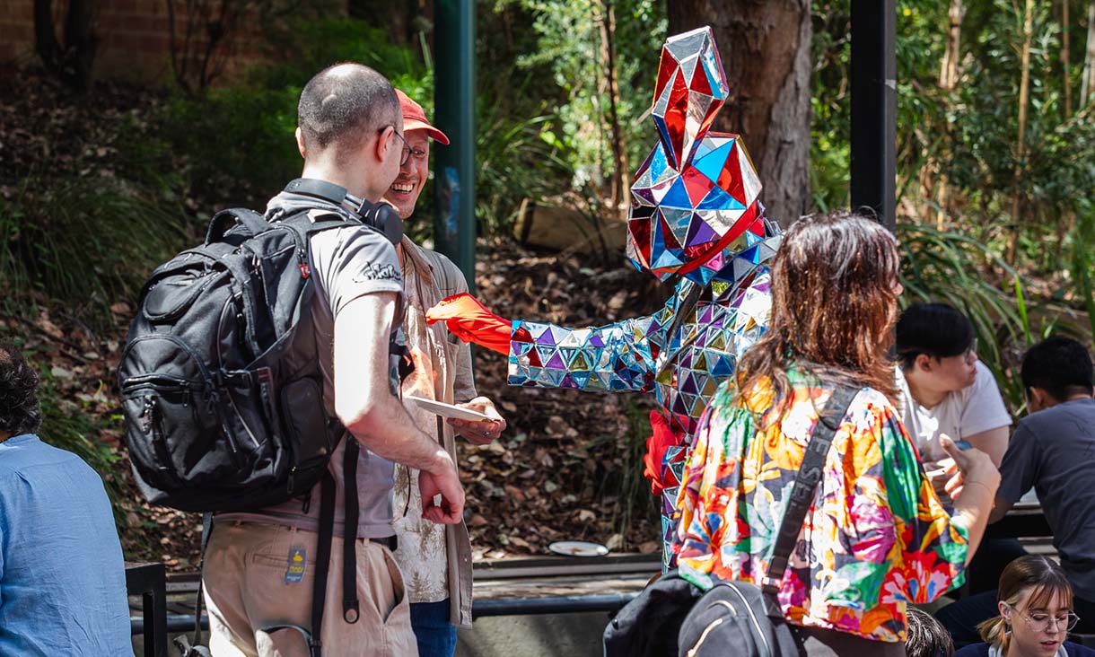 Person dressed in colorful costume interacts with two people.