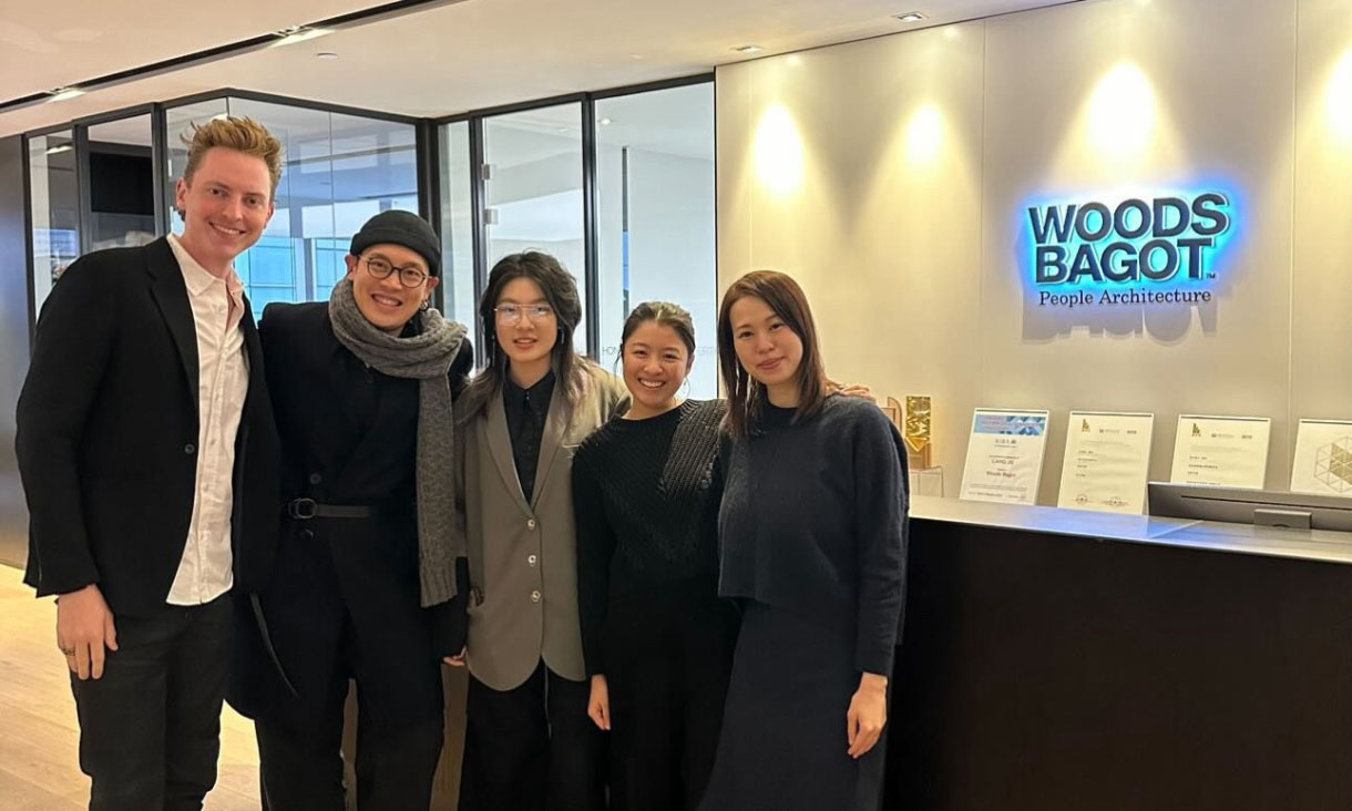 Five people stand in front of a blue 'Woods Bagot' sign.