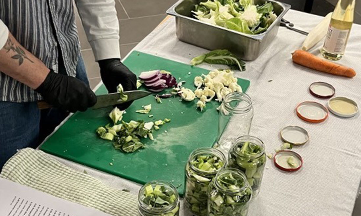 A mans hands in black gloves holding a knife dicing up food on a green chopping board.