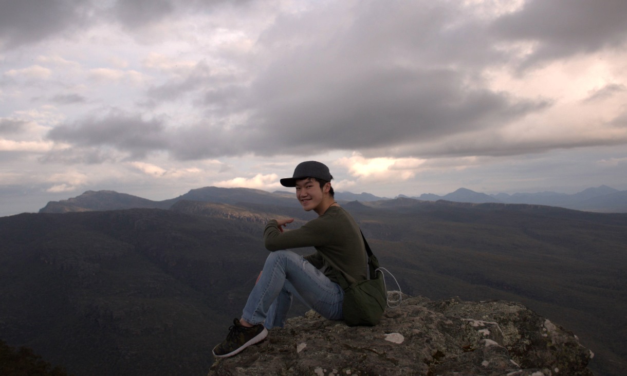 Person sits on a rocky surface with mountains in the background.