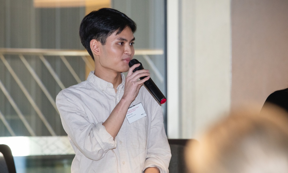 Student standing with microphone presenting a speech to a small group. 