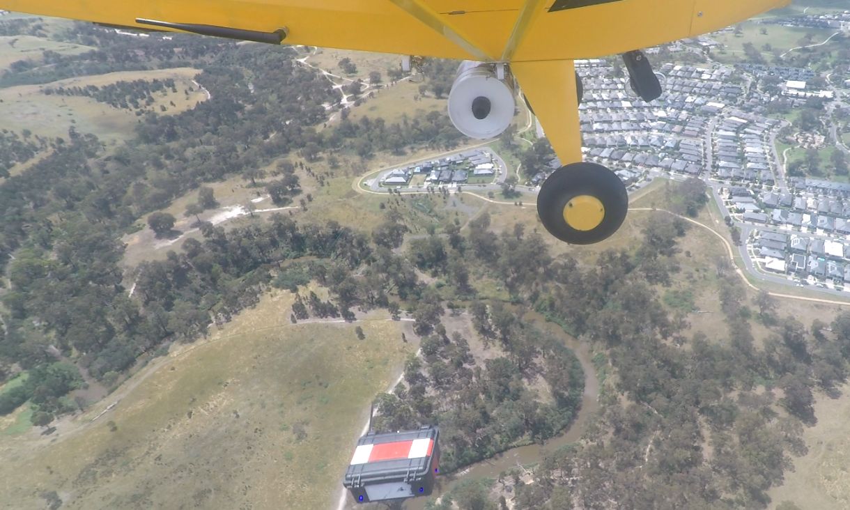 Photo of a yellow airplan dropping a small packing over green fields.