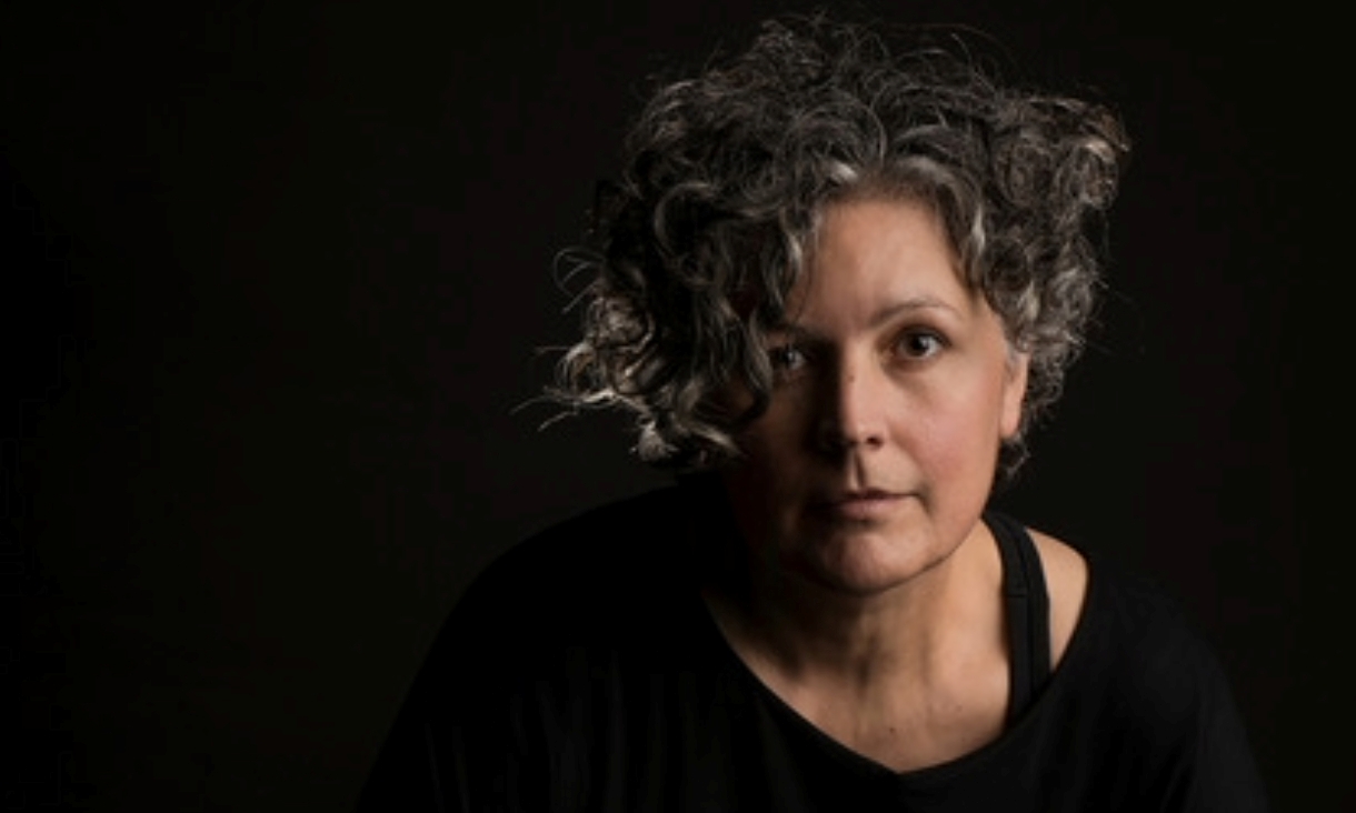 Portrait of woman staring at camera in front of a black background.