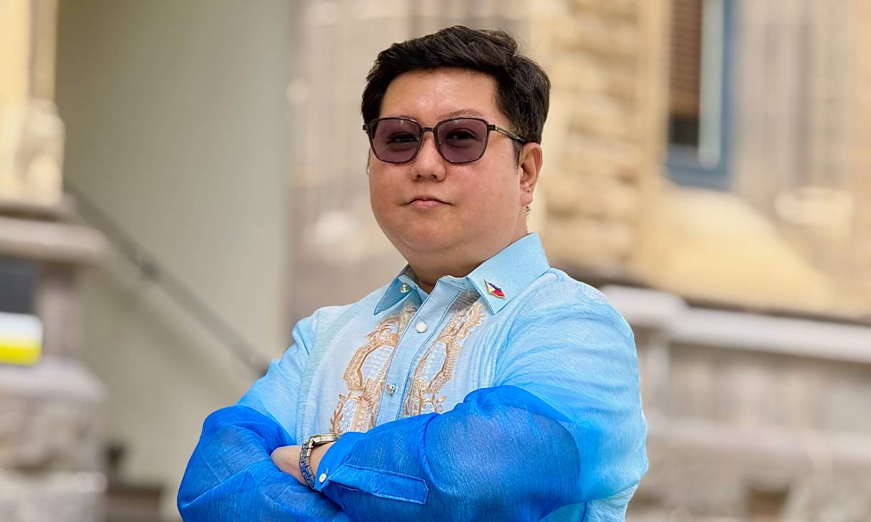 Man standing with arms crossed in front of stone building