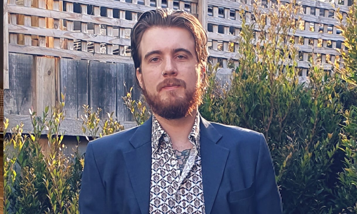 Man in blue suit standing in front of plants posing for a photo.