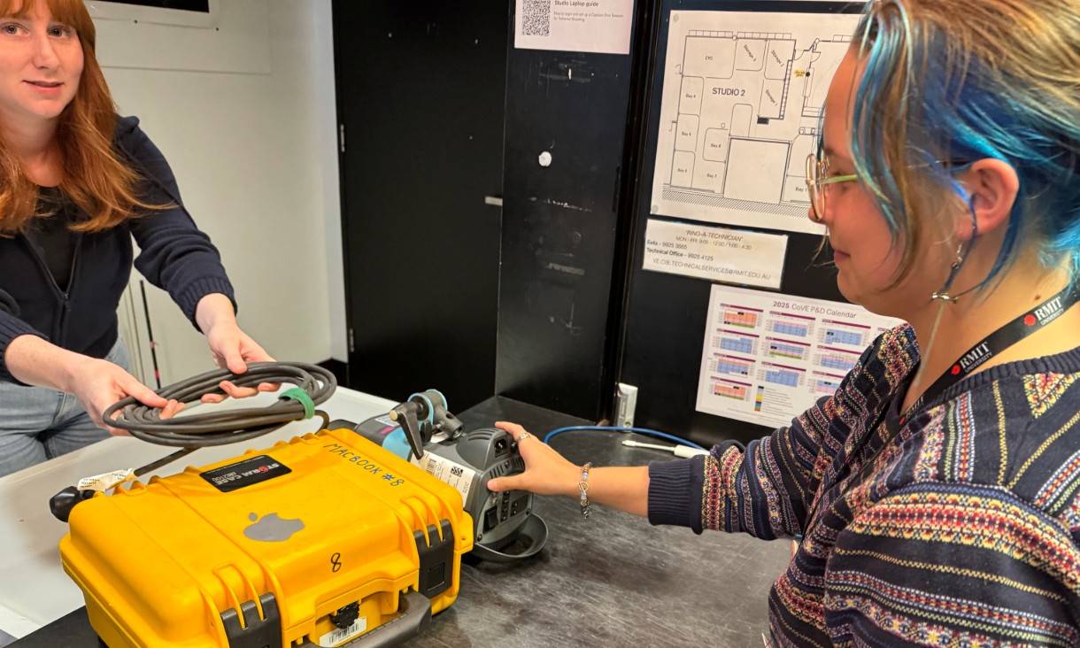 Two people standing over a desk holding work tools.