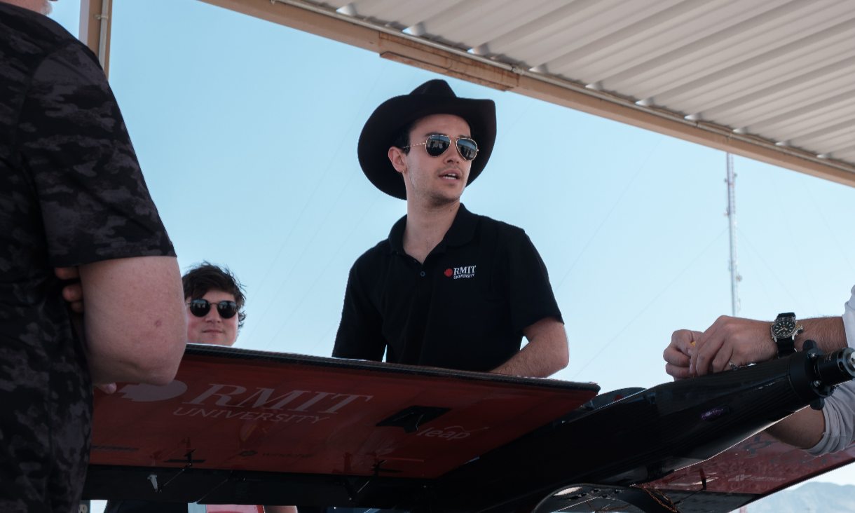 Ari outside at the competition wearing a hat and talking to the team.