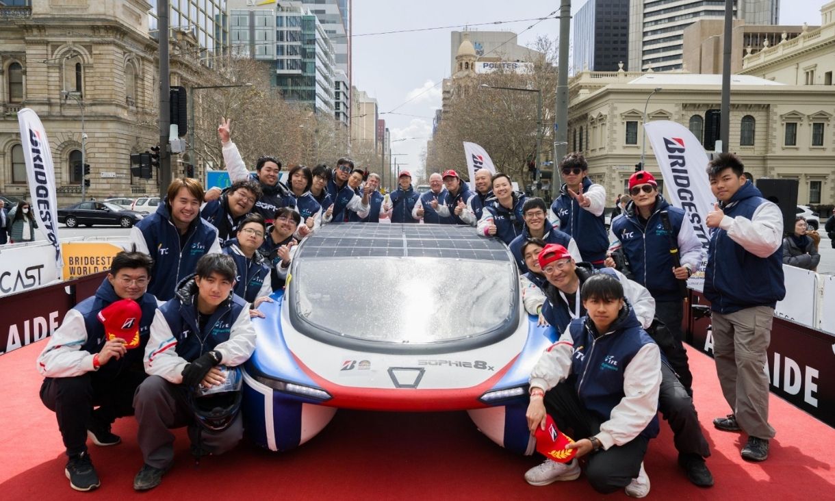 Group of people standing around solar car smiling