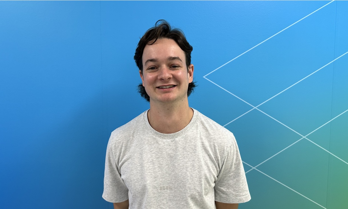 Portrait of an RMIT student standing against a blue and green geometric wall, wearing a light grey T-shirt.