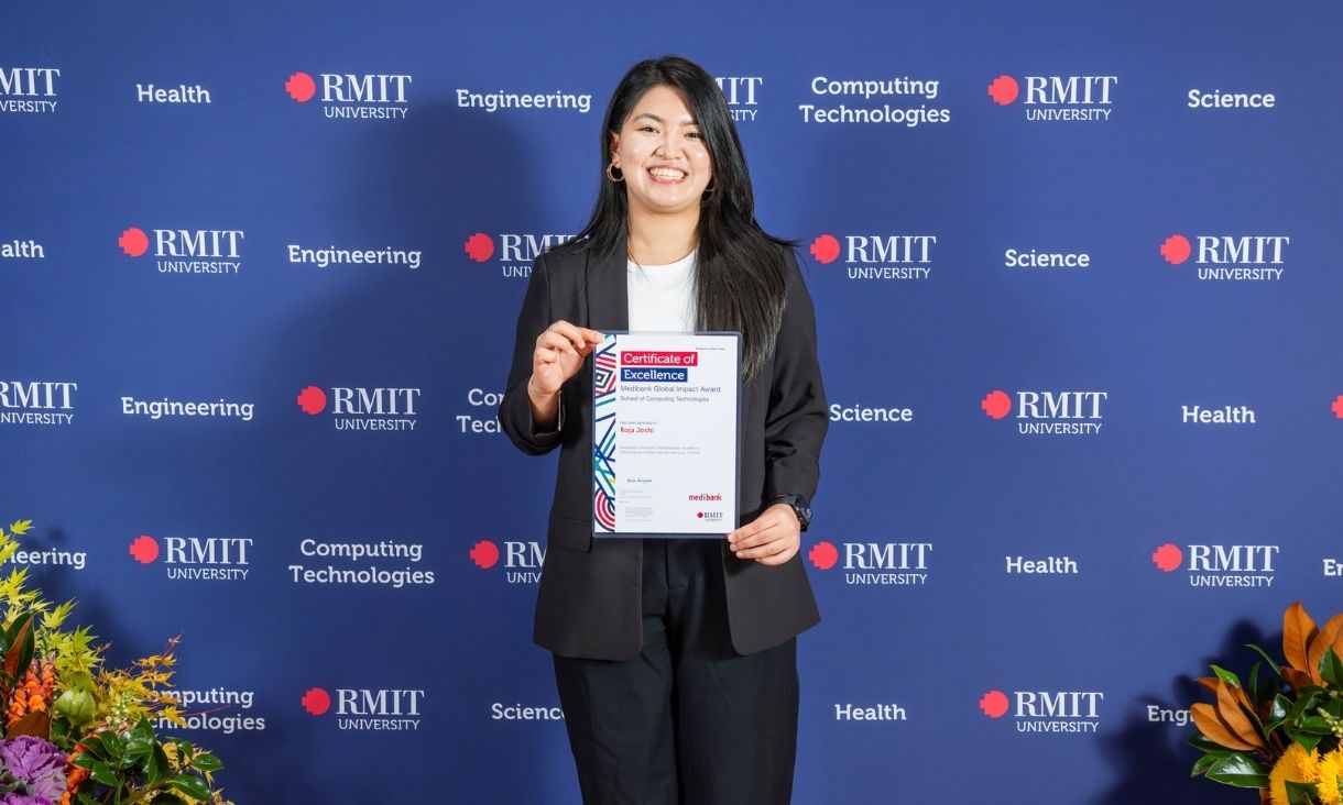 Student standing in front of RMIT media wall smiling while holding an award