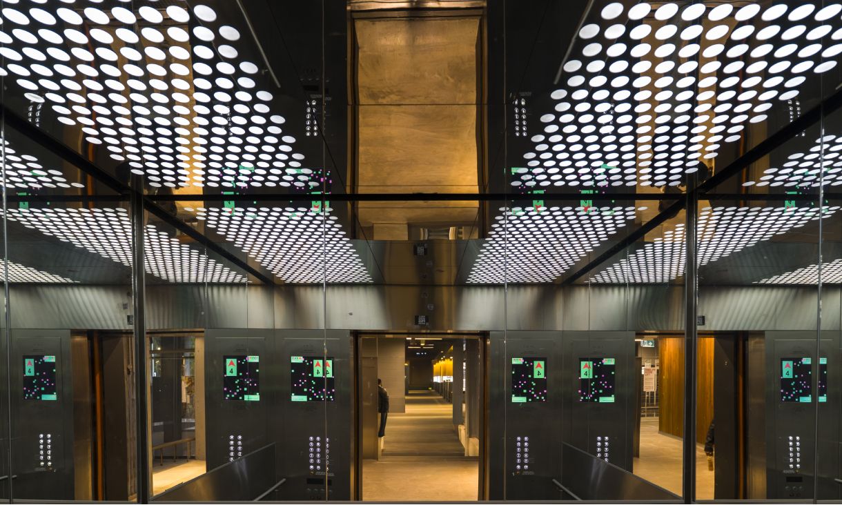 Interior of a lift in Building 10 at RMIT with mirrored walls, showing multiple screens displaying graphic elements from Artificial Intelligelism.