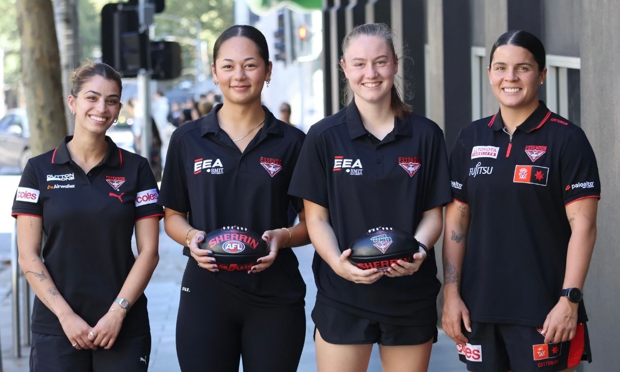 Four people holding footballs standing outside