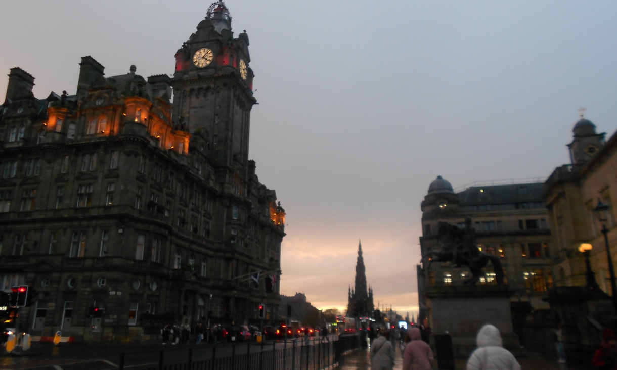 The Balmoral Hotel clock tower and Scott Monument along a rain-soaked Princes Street in Edinburgh at dusk.