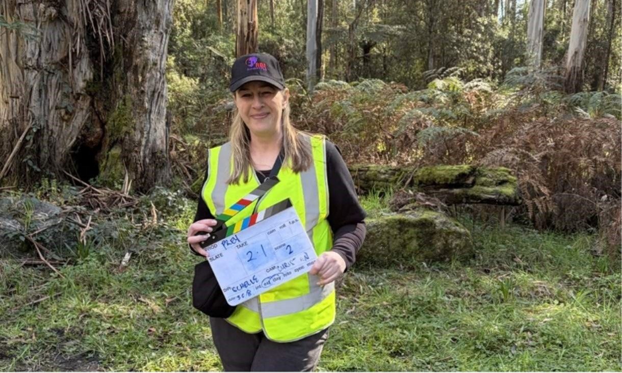 Danielle standing in forrest with a hi-vis vest holding a slate