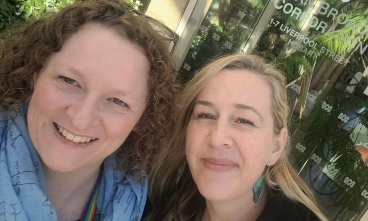 Two women standing next to eachother smiling at camera