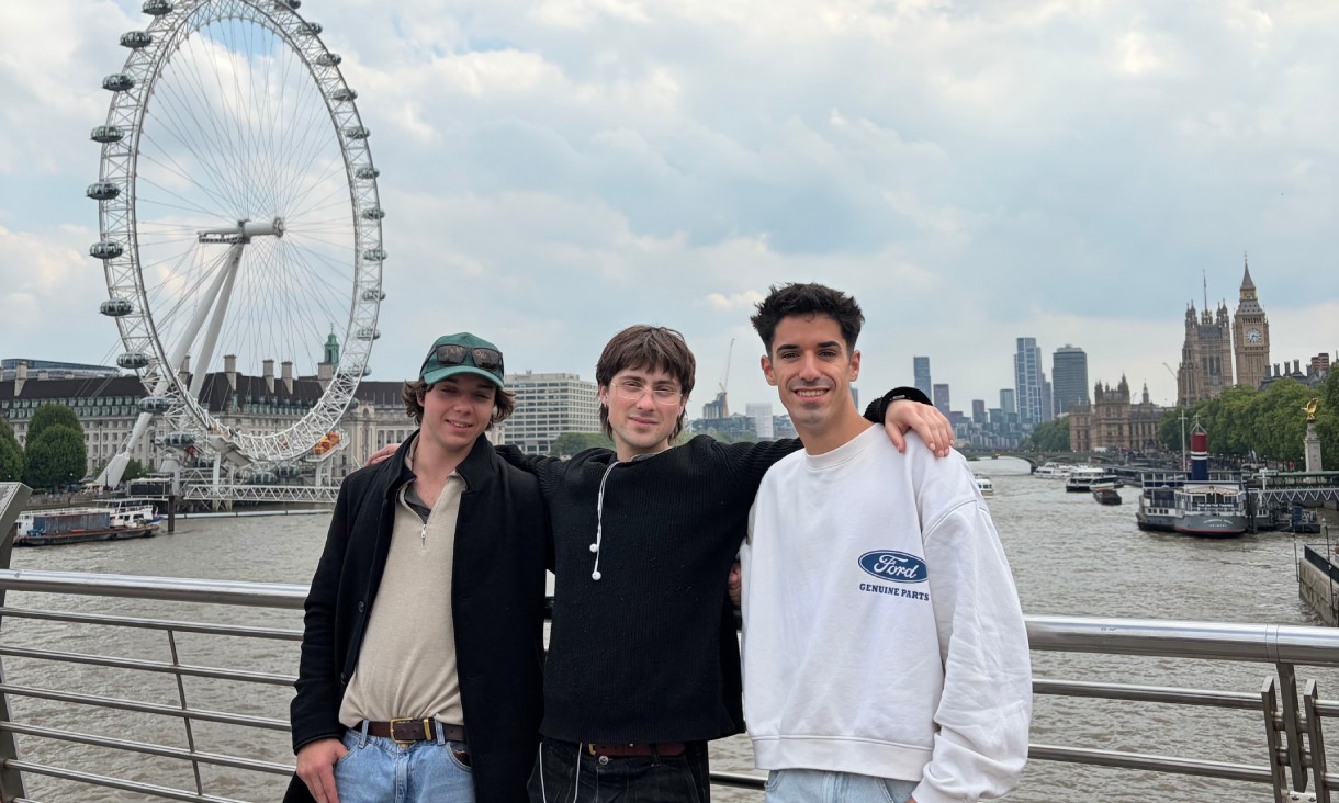 Three people standing beside the River Thames, with the London Eye and Palace of Westminster visible in the background.
