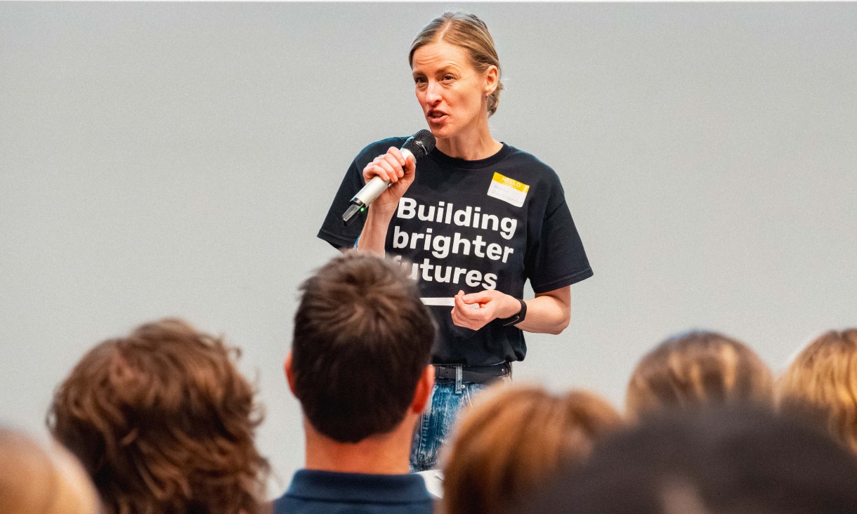 Bianca from Kids Under Cover speaks into a microphone in front of students at the summit.