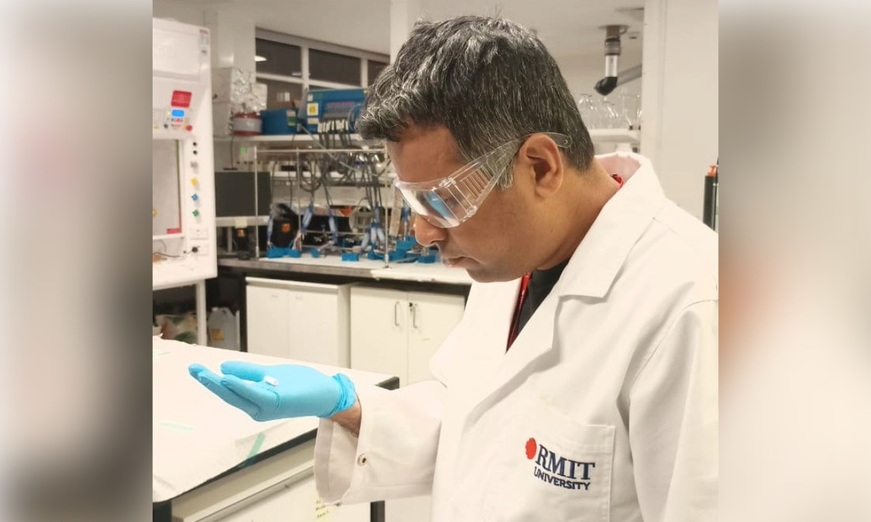 Mustafijur Rahman in a lab coat and safety glasses examining a small sample on his gloved hand.