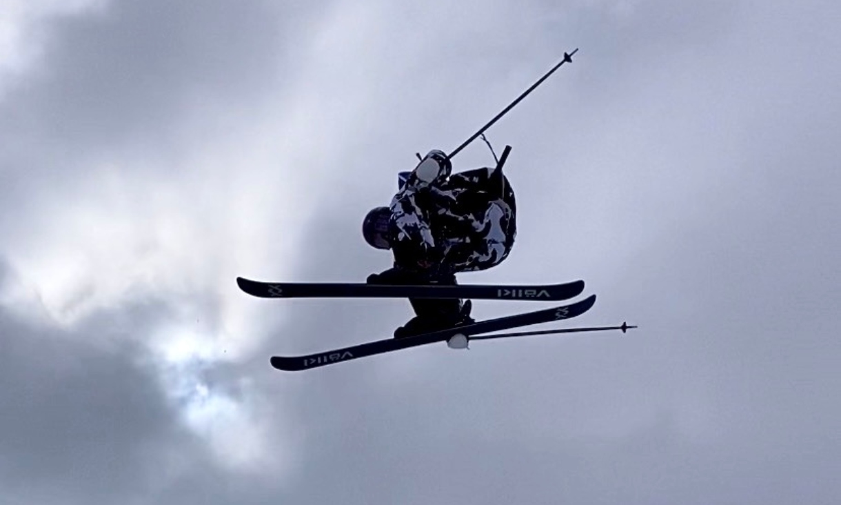 Freestyle skier performing an aerial manoeuvre against a cloudy sky.