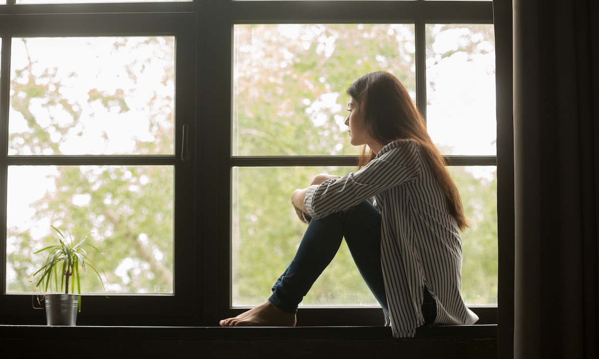 Girl sitting on window sill looking forlorn.