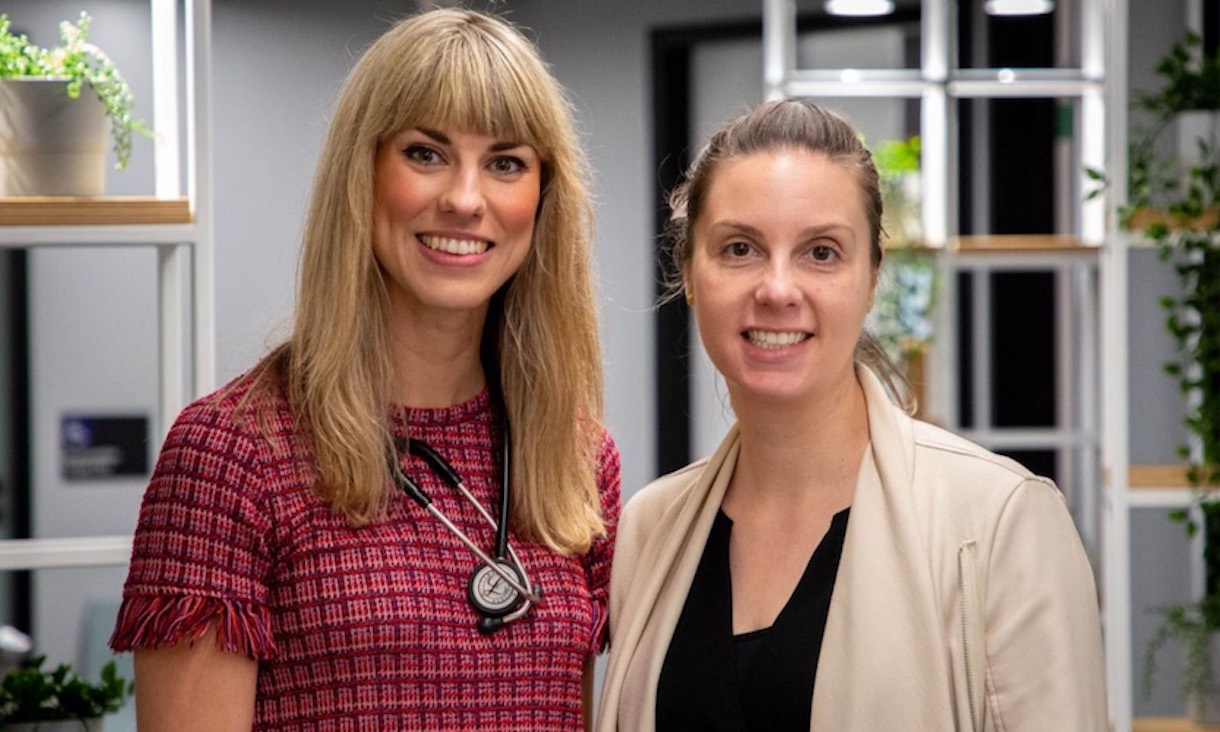 Two women stand in a medical clinic smiling at the camera.