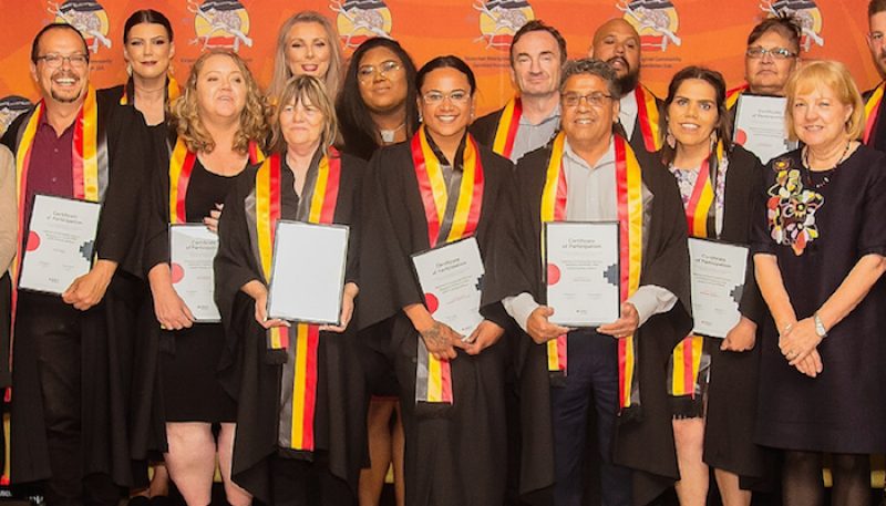 Students wearing indigenous sashes stand with their testamurs.
